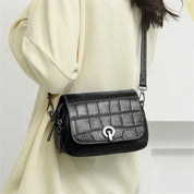 Borsa a tracolla donna in pelle nera con texture coccodrillo, chiusura a gancio, indossata su abito chiaro. Accessorio moda elegante e versatile.