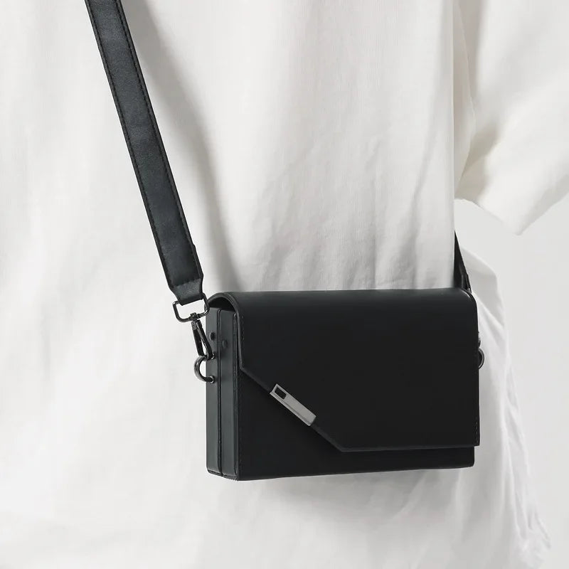Borsa a tracolla nera in pelle, design minimalista, chiusura a patta, indossata su maglietta bianca. Accessorio moda elegante e versatile.