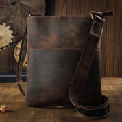 Borsa a tracolla in pelle marrone vintage su tavolo di legno, design elegante e resistente, ideale per uomo, accessorio moda casual.