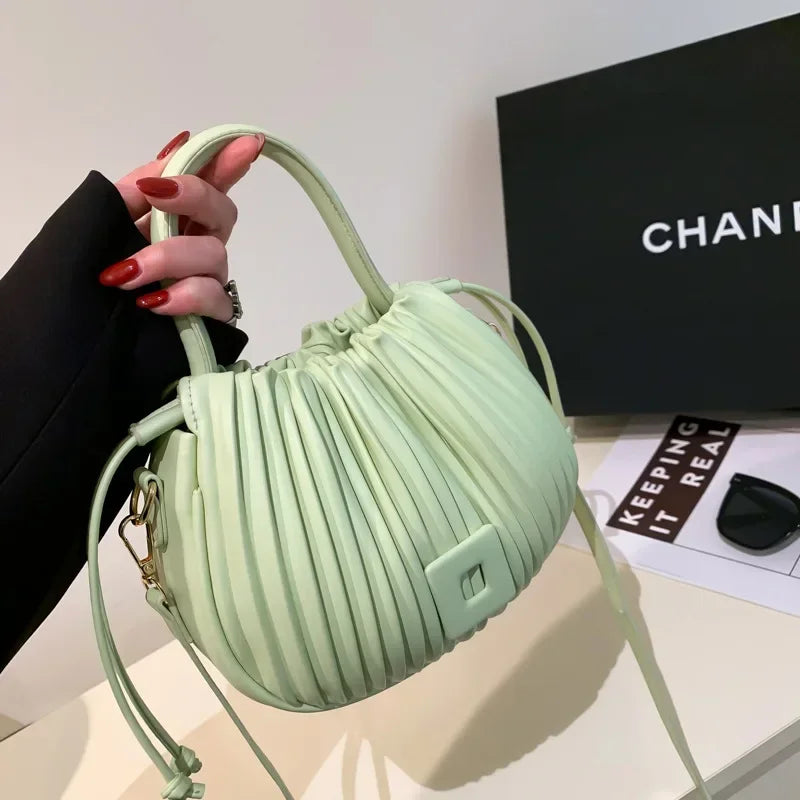 Borsa a mano verde menta plissettata, design elegante, con manico e tracolla. Sfondo con scatola nera e occhiali da sole. Accessorio moda chic.