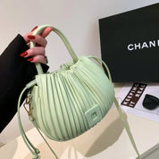 Borsa a mano verde menta plissettata, design elegante, con manico e tracolla. Sfondo con scatola nera e occhiali da sole. Accessorio moda chic.