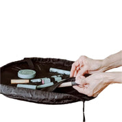 Mani che organizzano trucchi in una borsa cosmetica nera aperta, contenente rossetti, pennelli e prodotti di bellezza. Accessori make-up portatili.