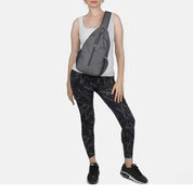 Donna con borsa a tracolla grigia, indossa top bianco, leggings neri marmorizzati e scarpe da ginnastica nere. Moda casual, accessori pratici.