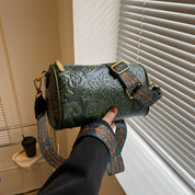 Borsa a tracolla cilindrica verde con motivo floreale in rilievo, fibbia dorata e tracolla decorata. Accessorio moda elegante e versatile.