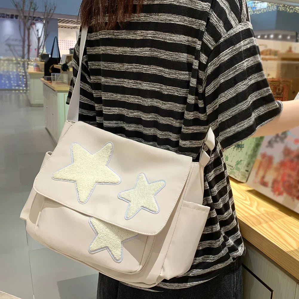 Borsa a tracolla bianca con stelle ricamate, indossata da una persona in maglietta a righe. Accessorio moda casual, ideale per shopping e uscite.