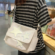 Borsa a tracolla bianca con stelle ricamate, indossata da una persona in maglietta a righe. Accessorio moda casual, ideale per shopping e uscite.