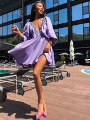 Donna in abito viola chiaro con scollo profondo, posa vicino a piscina all'aperto. Moda estiva, eleganza, stile moderno.