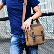 Uomo con borsa a tracolla in tela marrone, stile casual, indossa jeans e maglietta blu. Accessorio moda maschile, ideale per uso quotidiano.