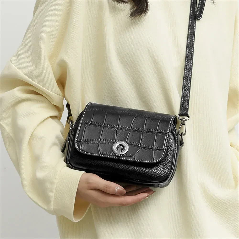 Borsa a tracolla nera in pelle con texture coccodrillo, chiusura a fibbia argentata, indossata su maglia chiara. Accessorio moda elegante e versatile.