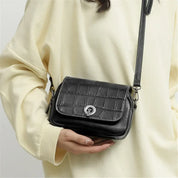 Borsa a tracolla nera in pelle con texture coccodrillo, chiusura a fibbia argentata, indossata su maglia chiara. Accessorio moda elegante e versatile.