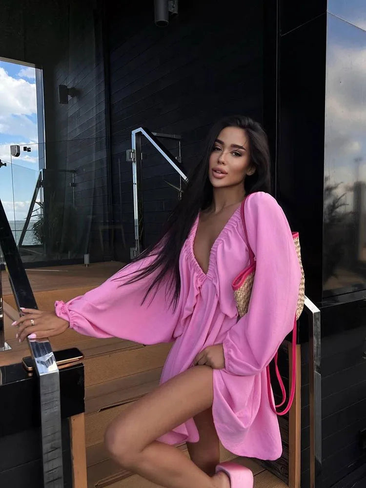 Donna con abito rosa a maniche lunghe, scollatura a V, posa su scala moderna. Moda estiva, stile elegante, abbigliamento femminile trendy.