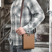 Uomo con camicia a quadri grigia indossa borsa a tracolla in pelle marrone, stile casual urbano, moda maschile, accessorio pratico e moderno.