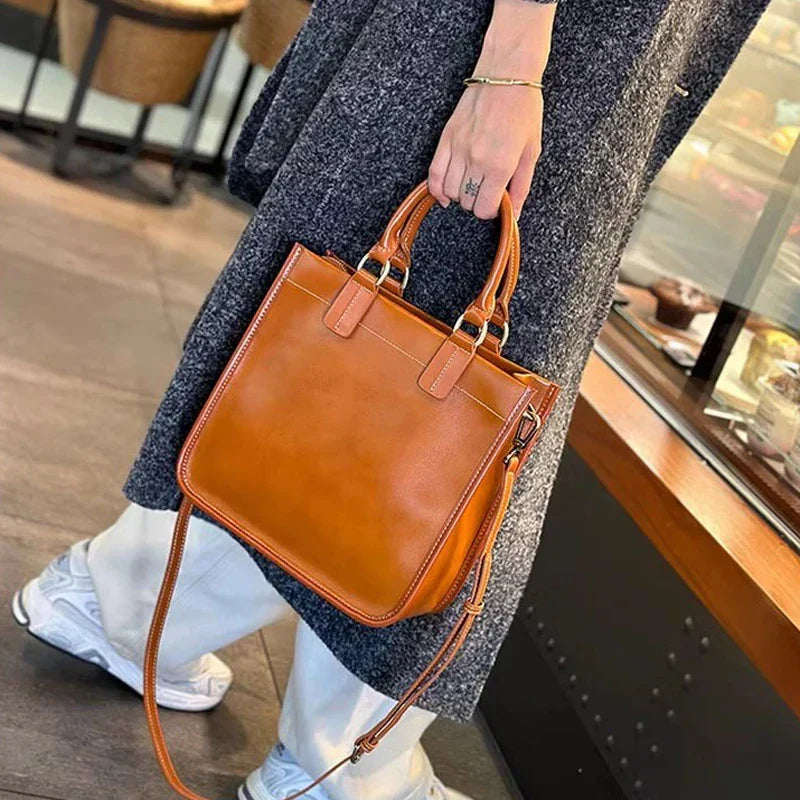 Borsa a mano in pelle marrone, elegante e moderna, indossata da una persona in cappotto grigio. Accessorio moda donna, stile casual chic.