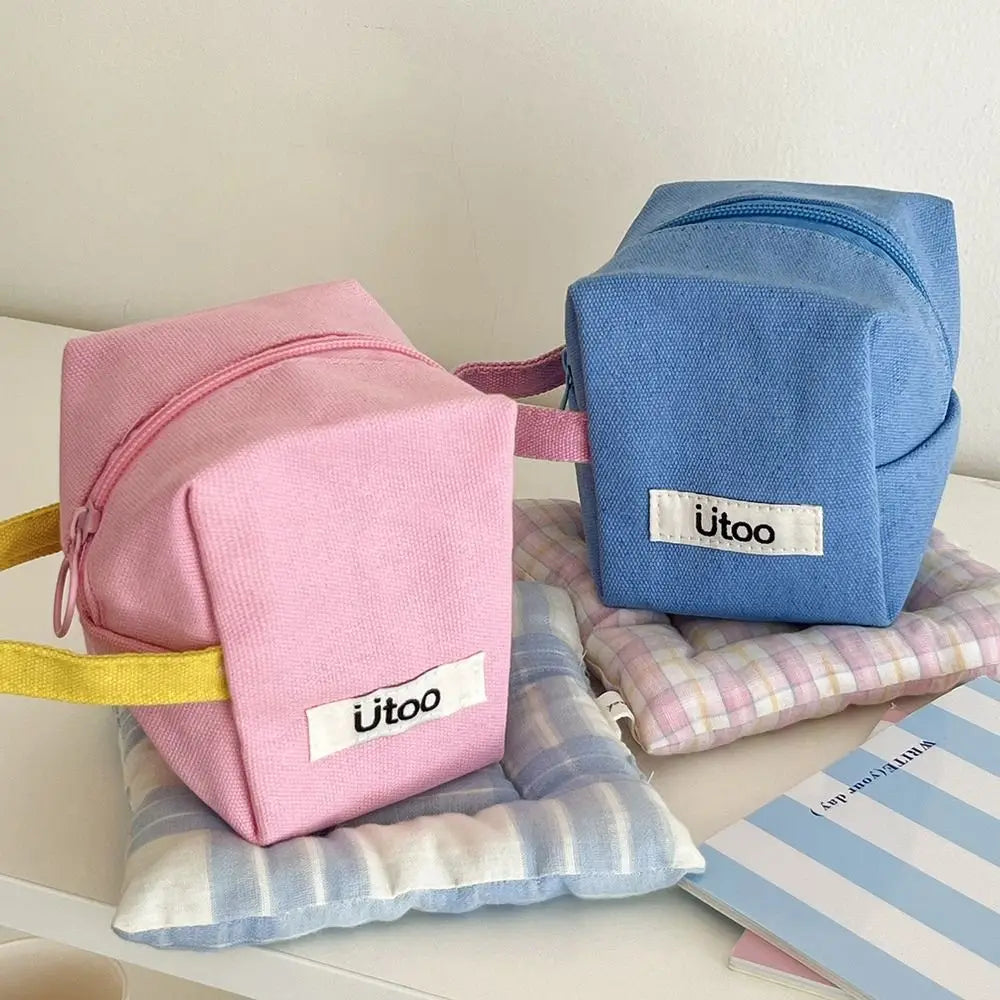 Due astucci in tessuto, uno rosa e uno blu, con cerniera e logo "Ütoo", su cuscini a quadretti. Accessori scuola, organizer trucco.