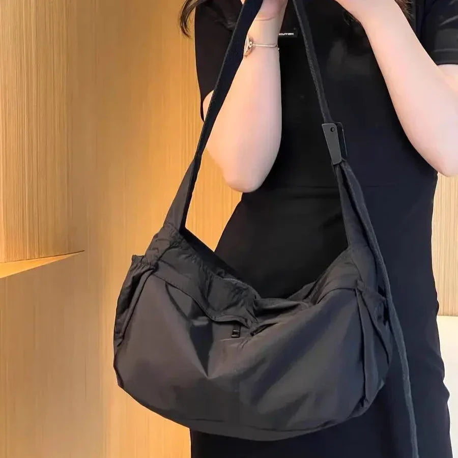 Borsa a tracolla nera in tessuto, design moderno, indossata da una donna in abito nero. Accessorio moda elegante e versatile per ogni occasione.
