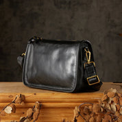 Borsa a tracolla in pelle nera su tavolo di legno, design elegante con fibbie dorate. Accessorio moda donna, stile classico e raffinato.
