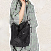 Camicia a quadri verde e borsa a tracolla nera in nylon con tasca frontale, indossata da una persona. Accessorio moda casual e pratico.