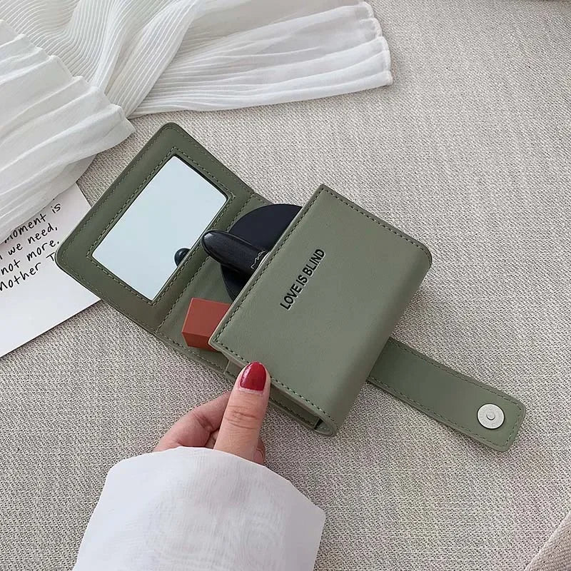 Portafoglio verde in pelle con specchio integrato, chiusura a bottone, design compatto. Accessorio moda elegante per donna, perfetto per organizzare trucchi.