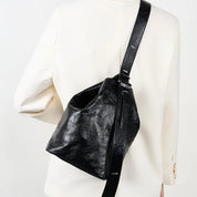 Borsa a tracolla nera in pelle, design moderno, indossata su giacca bianca. Accessorio moda elegante, ideale per look casual e formali.