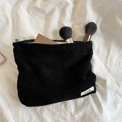 Astuccio nero in velluto a coste con cerniera, contenente pennelli da trucco e una palette. Accessorio cosmetico elegante su sfondo bianco.