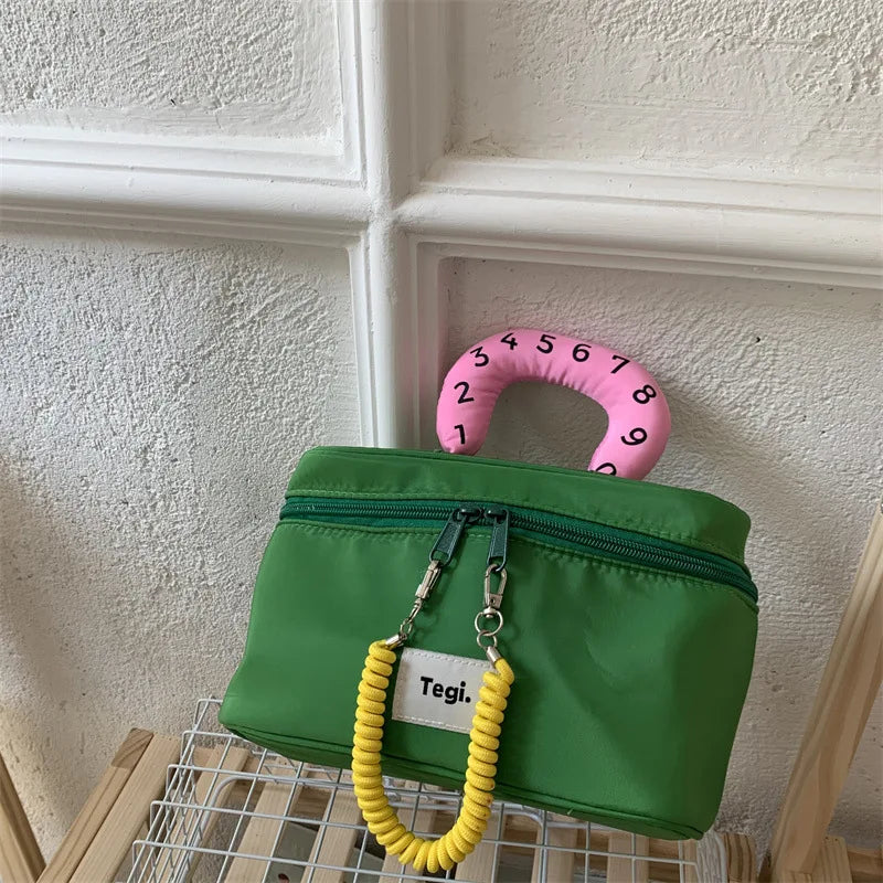 Borsa verde con manico rosa numerato, design moderno, chiusura a zip, decorazione gialla. Accessorio moda unico e colorato.
