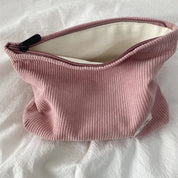 Borsa cosmetica in tessuto a coste rosa con cerniera aperta, su sfondo bianco. Accessorio moda, organizer da viaggio, elegante e pratico.