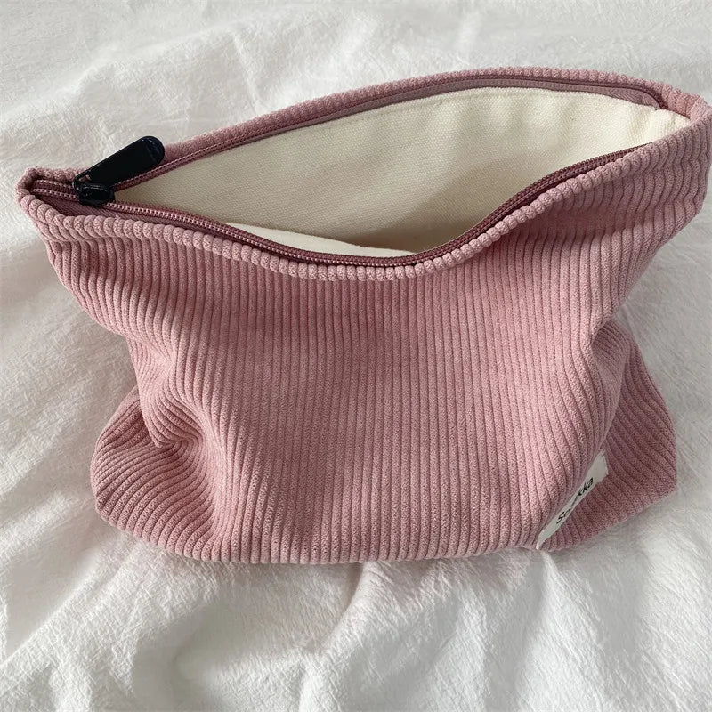 Borsa cosmetica in tessuto a coste rosa con cerniera aperta, su sfondo bianco. Accessorio moda, organizer da viaggio, elegante e pratico.