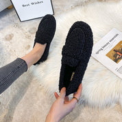Scarpe mocassini donna in pelliccia sintetica nera, su tappeto bianco. Design elegante e confortevole, perfetto per moda autunno-inverno.