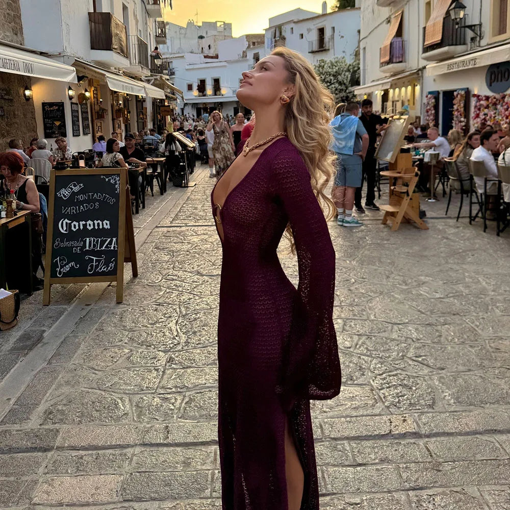 Donna in abito lungo viola passeggia in una strada affollata di ristoranti all'aperto al tramonto, Ibiza. Atmosfera estiva, moda elegante.