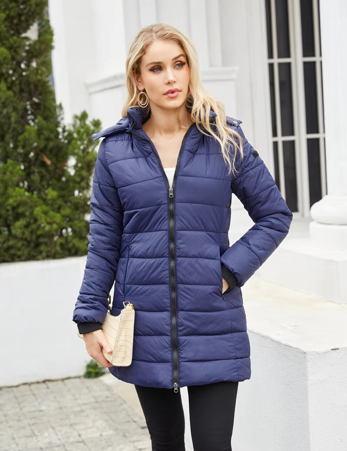 Donna con cappotto invernale blu trapuntato, chiusura a zip, tasche laterali, sfondo urbano. Cappotto caldo, moda donna, abbigliamento invernale.