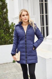 Donna con cappotto invernale blu trapuntato, chiusura a zip, tasche laterali, sfondo urbano. Cappotto caldo, moda donna, abbigliamento invernale.