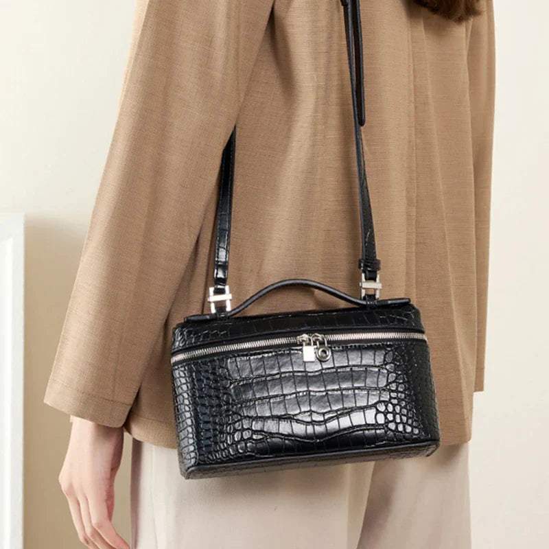 Borsa a tracolla nera in pelle effetto coccodrillo, chiusura con zip e fibbia argentata, indossata su cappotto beige. Accessorio moda elegante.