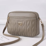 Borsa a tracolla beige in pelle sintetica con motivo trapuntato, cerniera dorata e decorazione a cuore intrecciato. Elegante e moderna.