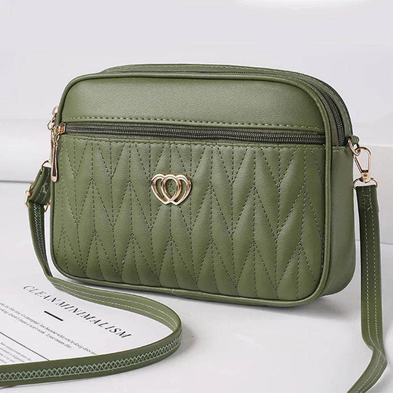 Borsa a tracolla verde oliva in pelle sintetica con motivo trapuntato, cerniera dorata e decorazione a cuore. Accessorio moda elegante e pratico.