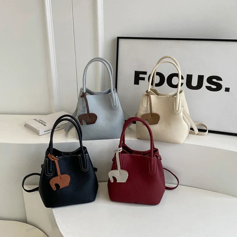 Quattro borse a mano eleganti in pelle, colori nero, grigio, rosso e bianco, con charm decorativo, su sfondo bianco minimalista.