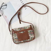 Borsa a tracolla floreale vintage con dettagli in pelle marrone, occhiali e rivista su sfondo bianco. Accessorio moda donna elegante e retrò.