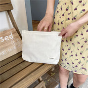 Donna con abito giallo a fiori tiene una borsa a tracolla bianca in tessuto a coste. Accessorio moda estivo, stile casual chic.