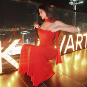 Donna in abito rosso elegante su terrazza illuminata, sfondo urbano notturno. Moda serale, abbigliamento femminile, stile glamour.