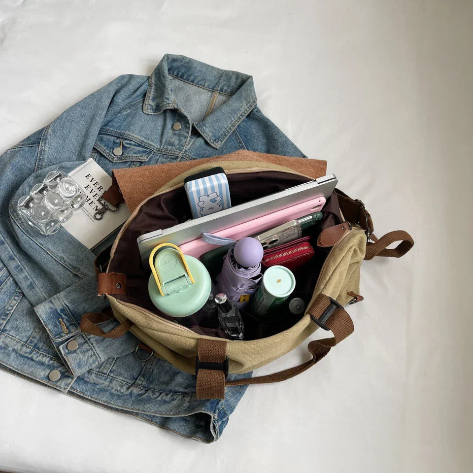 Borsa beige aperta su giacca di jeans, contenente laptop, bottiglia d'acqua, portafoglio, astuccio e accessori. Accessori moda casual.