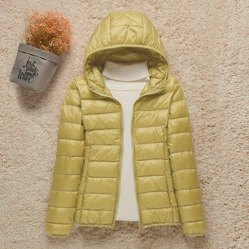 Giacca invernale donna gialla con cappuccio, imbottita, su sfondo beige. Moda autunno-inverno, abbigliamento caldo e casual.