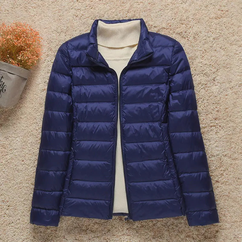 Giacca invernale trapuntata blu scuro da donna su sfondo beige, con collo alto e chiusura a zip. Elegante e calda, ideale per l'inverno.