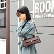 Donna con cappotto azzurro indossa borsa a tracolla marrone in pelle, design elegante e moderno, perfetta per ufficio e uso quotidiano.