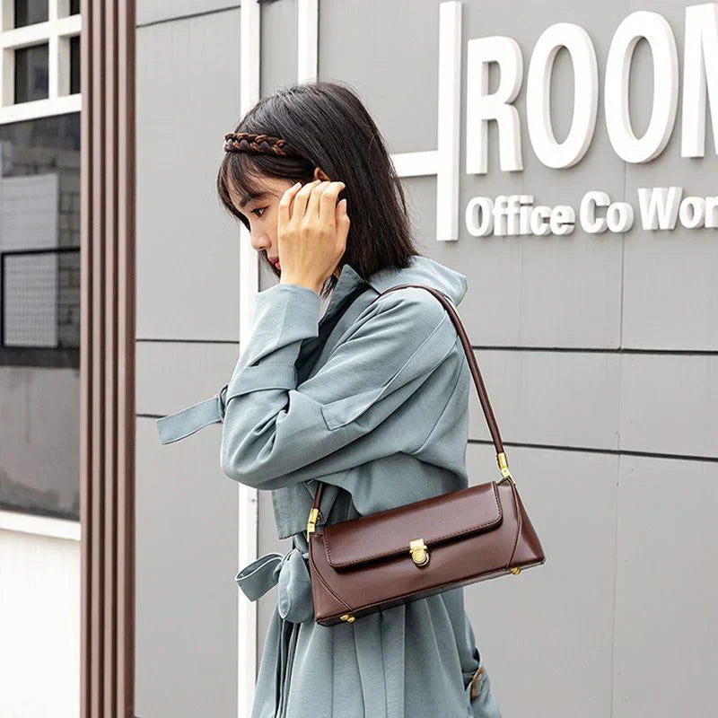 Donna con cappotto azzurro indossa borsa a tracolla marrone in pelle, design elegante e moderno, perfetta per ufficio e uso quotidiano.