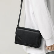 Borsa a tracolla nera in pelle, design minimalista, indossata su maglia bianca. Accessorio moda elegante e versatile per uomo e donna.