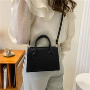 Borsa a tracolla nera elegante indossata da donna con camicetta bianca. Design moderno, ideale per moda casual e formale. Accessorio di tendenza.