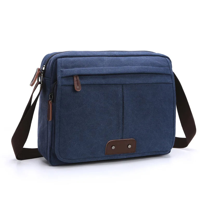 Borsa a tracolla in tela blu con tasche frontali, chiusura a zip e dettagli in pelle marrone. Design casual, ideale per uomo e donna.