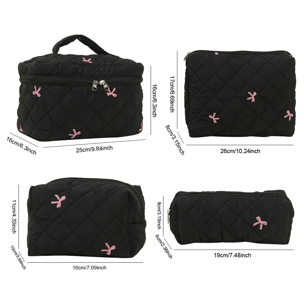 Set di borse da viaggio nere trapuntate con fiocchi rosa, diverse dimensioni, chiusura a zip, ideali per cosmetici e accessori.