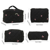 Set di borse da viaggio nere trapuntate con fiocchi rosa, diverse dimensioni, chiusura a zip, ideali per cosmetici e accessori.