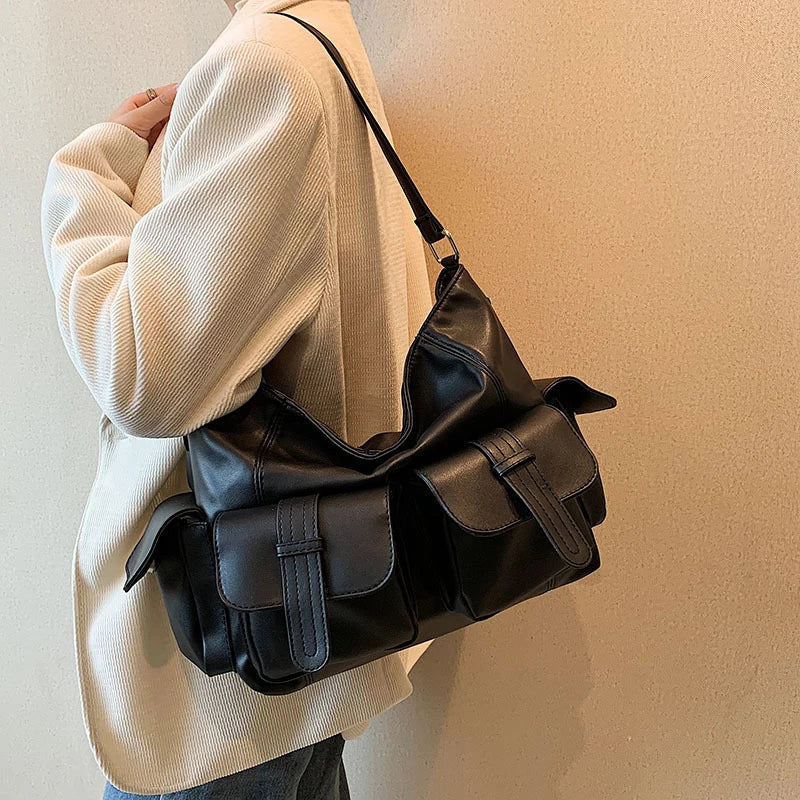 Borsa a tracolla nera in pelle con tasche multiple, indossata su giacca beige. Design elegante e funzionale, ideale per moda urbana e casual.