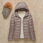Giacca invernale trapuntata da donna con cappuccio, colore grigio, su sfondo beige. Moda femminile, abbigliamento caldo, stile casual.
